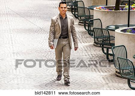 Stock Image - Hispanic businessman walking in courtyard. Fotosearch