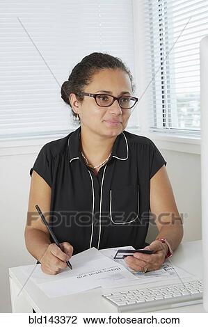 Stock Image - Hispanic businesswoman shopping online at desk. Fotosearch