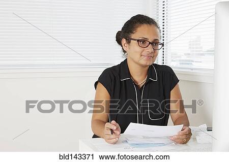 Stock Image - Hispanic businesswoman working at desk. Fotosearch