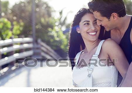 Picture - Hispanic couple hugging outdoors. Fotosearch