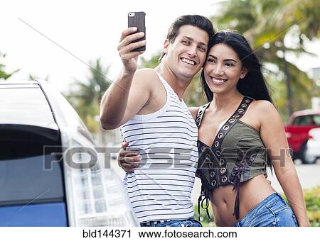 Stock Image - Hispanic couple taking cell phone selfie outdoors. Fotosearch