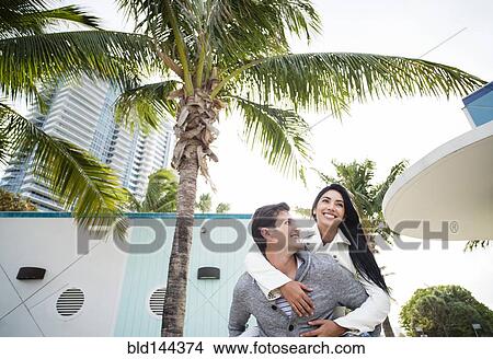 Picture - Hispanic man carrying girlfriend piggyback outdoors. Fotosearch