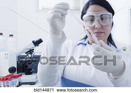Stock Image - Hispanic scientist pipetting blood sample in laboratory. Fotosearch