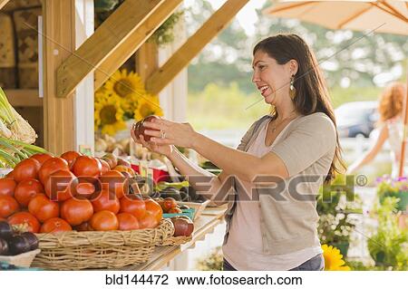 Stock Image - Hispanic woman browsing fruit at farmers market. Fotosearch