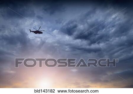 Stock Image - Low angle view of helicopter flying in cloudy sky. Fotosearch