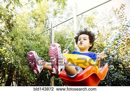 Stock Image - Low angle view of mixed race girl playing on swing. Fotosearch