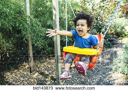 Stock Image - Low angle view of mixed race girl shouting on swing. Fotosearch
