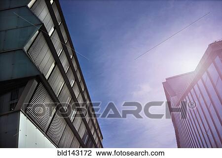Stock Image - Low angle view of sunbeams over modern buildings. Fotosearch