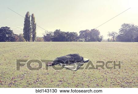 Stock Image - Man napping on coat in park field. Fotosearch