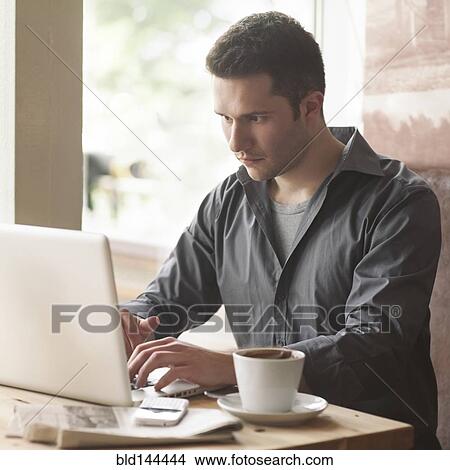 Picture - Man using laptop with cup of coffee in cafe. Fotosearch