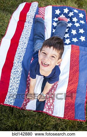 Stock Image - Mixed race boy laying on American flag blanket on grass. Fotosearch