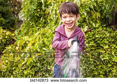 Stock Image - Mixed race boy playing with hose in garden. Fotosearch