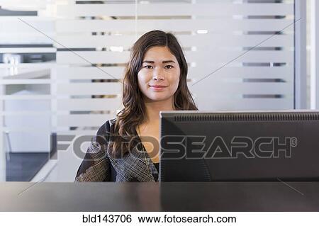 Stock Photograph - Mixed race businesswoman working at computer in office. Fotosearch