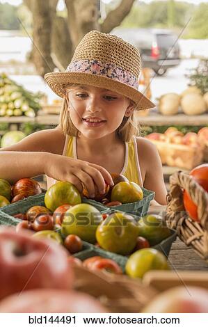 Stock Image - Mixed race girl browsing produce at farmers market. Fotosearch