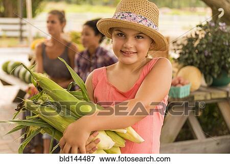 Stock Photo - Mixed race girl carrying corn stalks at farmers market. Fotosearch