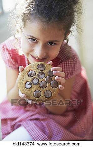 Picture - Mixed race girl eating large cookie. Fotosearch