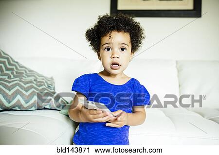 Stock Image - Mixed race girl using cell phone in living room. Fotosearch