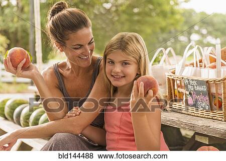 Mixed race mother and daughter holding fresh fruit at farmers market View Large Photo Image Stock Photo - Mixed race mother and daughter holding fresh fruit at farmers market. Fotosearch
