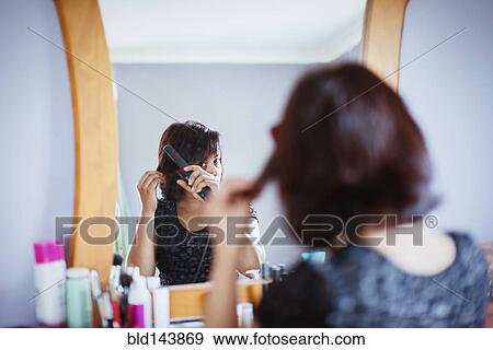 Stock Photo - Mixed race woman straightening hair in mirror. Fotosearch