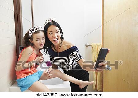 Mother and daughter taking cell phone selfie in tiaras in bathroom View Large Photo Image Stock Photo - Mother and daughter taking cell phone selfie in tiaras in bathroom. Fotosearch