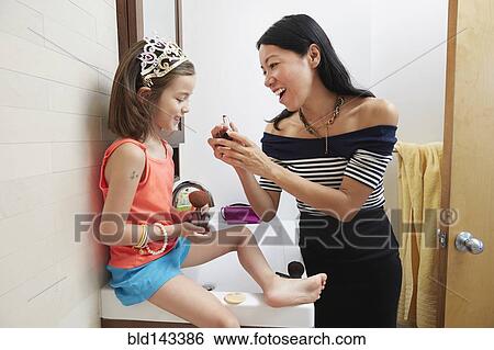 Stock Photograph - Mother teaching daughter to apply lipstick in bathroom. Fotosearch