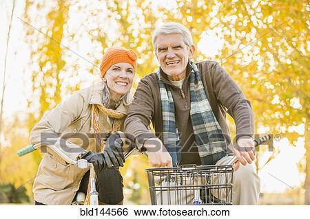 Stock Photograph - Older Caucasian couple riding bicycles near autumn trees. Fotosearch