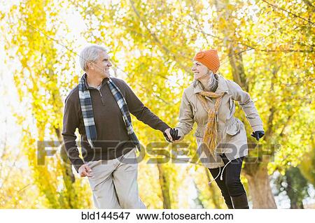 Stock Photo - Older Caucasian couple walking near autumn trees. Fotosearch