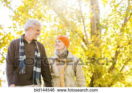 Stock Photograph - Older Caucasian couple walking near autumn trees. Fotosearch