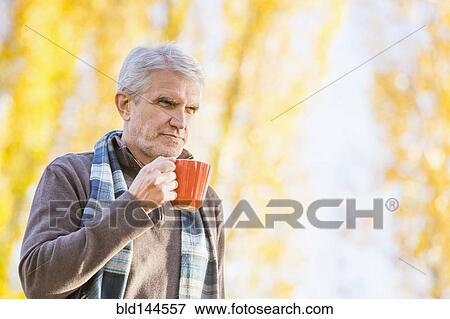 Stock Photo - Older Caucasian man drinking coffee near autumn trees. Fotosearch