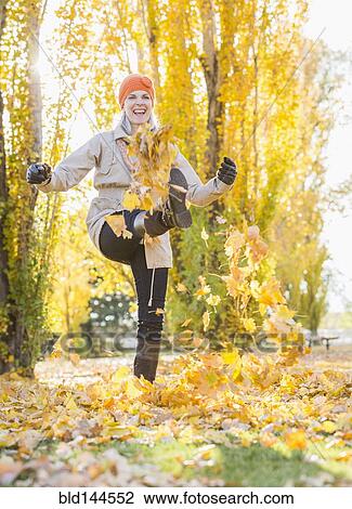 Stock Image - Older Caucasian woman kicking autumn leaves. Fotosearch