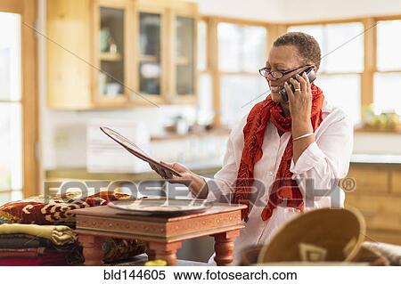 Stock Photography - Older mixed race woman talking on telephone in home office. Fotosearch