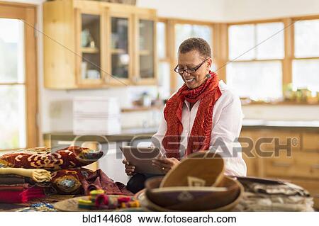 Stock Photo - Older mixed race woman using digital tablet in home office. Fotosearch