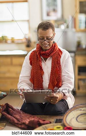 Stock Photo - Older mixed race woman using digital tablet in home office. Fotosearch