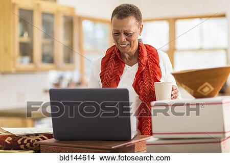 Picture - Older mixed race woman using laptop in home office. Fotosearch