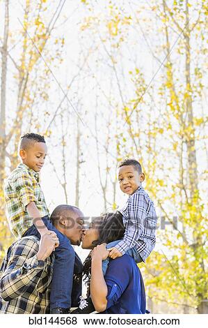 Stock Photo - Parents carrying children on shoulders near autumn trees. Fotosearch