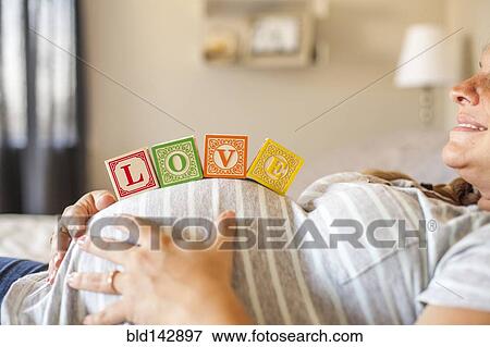 Stock Photo - Pregnant Caucasian woman balancing wooden blocks on her stomach in bed. Fotosearch