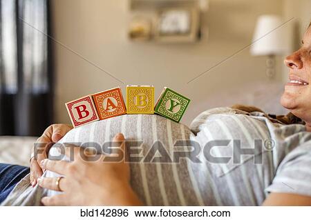 Stock Photograph - Pregnant Caucasian woman balancing wooden blocks on her stomach in bed. Fotosearch