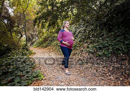 Pregnant Caucasian woman holding her stomach on forest path View Large Photo Image Picture - Pregnant Caucasian woman holding her stomach on forest path. Fotosearch