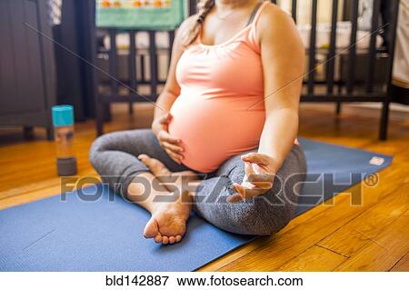 Stock Photo - Pregnant Caucasian woman meditating in nursery. Fotosearch