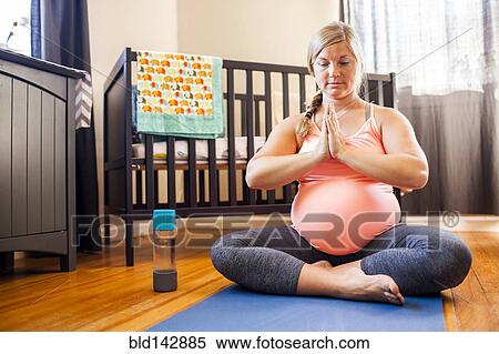 Stock Photography - Pregnant Caucasian woman meditating in nursery. Fotosearch