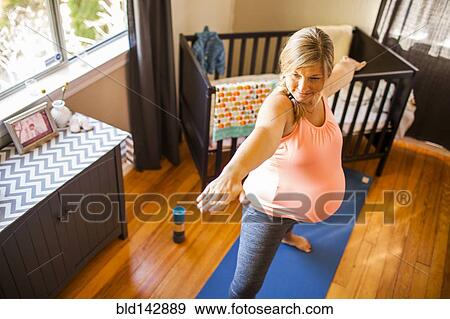 Stock Photo - Pregnant Caucasian woman practicing yoga in nursery. Fotosearch