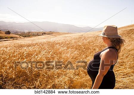 Picture - Pregnant Caucasian woman standing in rural meadow. Fotosearch