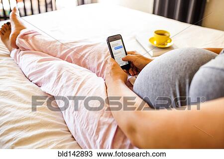Pregnant Caucasian woman using cell phone in bed View Large Photo Image Stock Image - Pregnant Caucasian woman using cell phone in bed. Fotosearch
