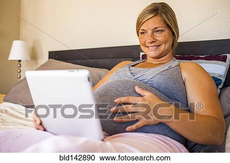 Pregnant Caucasian woman using digital tablet in bed View Large Photo Image Stock Image - Pregnant Caucasian woman using digital tablet in bed. Fotosearch