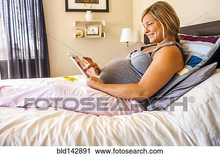Stock Image - Pregnant Caucasian woman using digital tablet in bed. Fotosearch