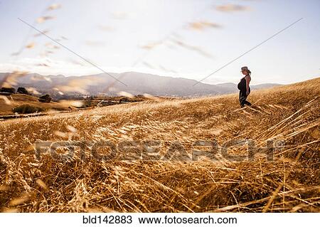 Stock Image - Pregnant Caucasian woman walking in rural meadow. Fotosearch