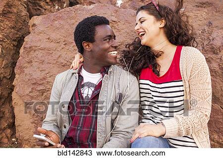 Stock Image - Smiling couple listening to earbuds together. Fotosearch