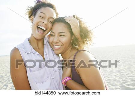 Stock Image - Smiling friends hugging at beach. Fotosearch