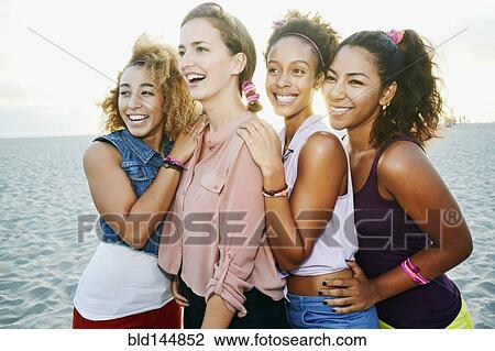 Stock Image - Smiling friends hugging at beach. Fotosearch