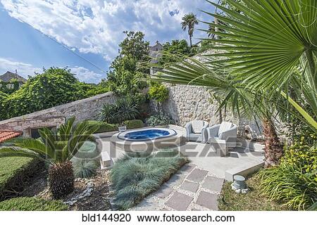 Stock Image - Soaking pool and armchairs on hillside patio. Fotosearch
